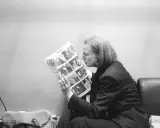 Fleur Jaeggy, con occhiali e giacca scura, legge un giornale con foto.