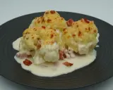 Tres porciones de coliflor gratinada con bechamel y trocitos de jamón, servidas en un plato oscuro.
