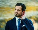 Prins Carl Philip i mörkblå kostym, vit skjorta och blå slips. Hans hand vilar bakom örat, en detalj som speglar hans intresse för carl philip design.