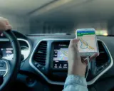 Mano al volante, móvil con mapa GPS mostrando cómo funciona un localizador GPS para coche.