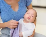 Un neonato con rigurgito, tenuto in braccio dalla madre che ha un panno viola.