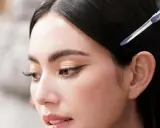 Primer plano de una mujer con ojos rasgados, delineado de gato y cabello oscuro recogido con una pinza.