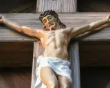 Jesus gekreuzigt, mit Dornenkrone und Wunden, hängt an einem Holzkreuz.