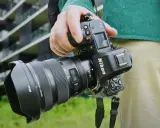 Dłoń trzyma aparat Nikon Z8 z obiektywem. W tle nowoczesny budynek.