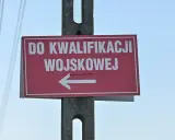 Czerwony znak z białym napisem "DO KWALIFIKACJI WOJSKOWEJ" i strzałką w lewo. Kategoria: d wojsko.
