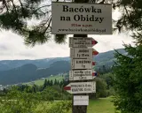 Tablica z drogowskazami na szlak na Radziejową. W tle górzysty krajobraz Beskidu Sądeckiego.