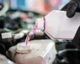 Mano con guante negro vierte líquido rosa, agua de motor coche, en depósito.