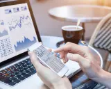 Manos revisando gráficos financieros en un teléfono móvil y portátil, gestionando el bbva net cash.