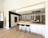 Cuisine moderne avec îlot central, plan de travail en bois et verrière industrielle. Une belle idée cuisine avec verriere pour un espace lumineux.
