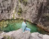 Mann sitzt auf Felsen am kristallklaren Wasser des Peneda-Gerês-Nationalparks.