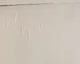 En vit vägg med bubblor och veck i tapeten, som om någon försökt tapetsera på tapet.