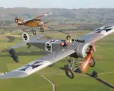 Zwei historische Fokker Eindecker fliegen über grüne Felder. Ein Pilot im Vordergrund, der andere im Hintergrund.