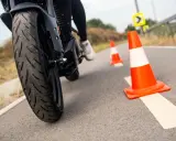 Motociclista practica maniobras entre conos naranjas. La rueda delantera de la moto, con su banda de rodadura, se ve de cerca.