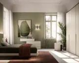 Camera da letto con accogliente **parete verde salvia**. Letto comodo, armadio capiente e un quadro astratto completano l'ambiente.