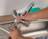 Mains de personne effectuant le montage robinet cuisine, connectant les tuyaux à l'évier.