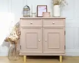 Meuble en bois peint en rose poudré, avec deux tiroirs et deux portes. Décoration florale et cage ornementale sur le dessus.