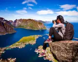 En fotograf fångar de dramatiska vyerna över Lofoten sevärdheter, med branta berg och en idyllisk by vid det blå havet.