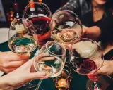 Hände heben Gläser mit Weiß- und Rotwein zum Anstoßen. Die ideale trinktemperatur für den Wein wird genossen.