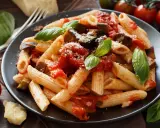 Un plato de pasta alla norma con penne, berenjena, salsa de tomate y albahaca fresca, espolvoreado con queso rallado.