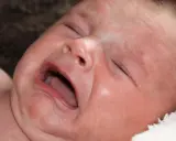 Ett kolikbarn gråter intensivt, med ögonen slutna och munnen öppen.
