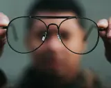 Osoba trzyma okulary przed twarzą. Chcesz wiedzieć, co zrobić, żeby nosić okulary?