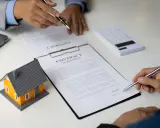 Podpisanie umowy dzierżawy domu. Obok modelu domu i kalkulatora, dwie osoby przy stole analizują dokumenty.