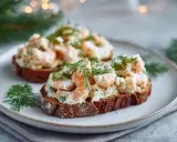 Två toast Skagen med dill och räkor på mörkt bröd, serverade på en tallrik.