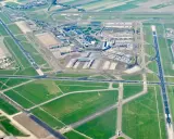 Ögonblicksbild över ams flygplats med flygplan på marken och i luften, omgivet av gröna fält och vägar.