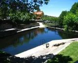 La piscina natural de Casas del Monte, rodeada de vegetación y con un edificio al fondo, invita a un refrescante baño.