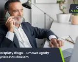 Uśmiechnięty mężczyzna rozmawia przez telefon, obok niego widoczny jest wzór umowy spłaty długu.