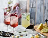 Orzeźwiające drinki na lato: malinowy z malinami i limonkowy z plasterkiem limonki, ozdobione lodem i miętą.