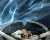 Aschenbecher mit Zigarettenstummeln und Rauchschwaden. Tipps, um Zigarettengeruch aus Wohnung zu entfernen.
