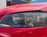 Faros sucios de coche rojo. El faro izquierdo muestra un anillo de luz, el derecho está rayado. La luz marcha atrás obligatoria es esencial para la seguridad.