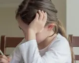 Dziewczynka z klasy 3 pisze dyktando, opierając głowę na dłoni.