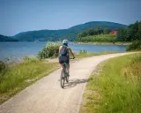 Kobieta na rowerze przemierza malowniczą trasę w Polsce, wzdłuż jeziora, podziwiając zielone wzgórza.