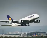 Samolot pasażerski Lufthansa z wysuniętym podwoziem startuje na tle lotniska.