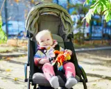 Uśmiechnięte dziecko w kolorowym sweterku i różowych skarpetkach siedzi w spacerówce, trzymając zabawkę. Od kiedy spacerówka stała się jego ulubionym miejscem na świecie.