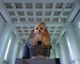 A colossal bust of an ancient Egyptian pharaoh, one of the museum's famous sculptures, stands majestically under a grand, coffered ceiling.