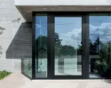 Puerta de entrada moderna con grandes ventanales de cristal, mostrando diferentes tipos de cristales para puertas exteriores que reflejan el cielo y la vegetación.