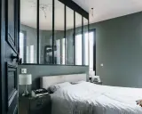 Agencement chambre moderne avec lit blanc, table de chevet industrielle et verrière séparant l'espace.