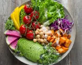 Une salade de crudités colorée et nutritive : avocat, tomates, pois chiches, patates douces, chou rouge, poivron jaune et pousses fraîches.