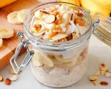 Słoik pełen pysznej owsianki z bananem, posypanej wiórkami kokosowymi i orzechami. Idealne śniadanie!