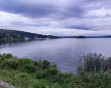 Spokojny zalew wióry, z łodziami przy brzegu i lasem w tle, pod burzliwym niebem.