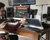 Un jeune sound engineer travaille dans son studio, entouré de matériel audio, d'écrans et d'un clavier.