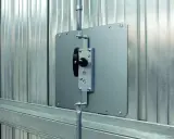 Système de verrouillage pour securiser porte garage. Poignée noire sur plaque métallique fixée sur porte en métal ondulé.