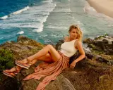 Elsa Pataky, con un top blanco y falda vaporosa, posa en rocas junto al mar.
