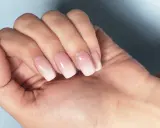 Dłoń z paznokciami w stylu francuski manicure, z delikatnym ombre od różu do bieli.