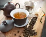 Dampfender Oolong Tee in einer Tasse, daneben Teekanne, Sieb und lose Teeblätter. Die Oolong Tee Wirkung kann belebend sein.