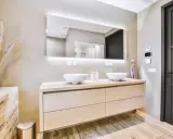 Elegantes baños modernos pequeños con lavabos dobles sobre mueble de madera clara, espejo iluminado y pared texturizada.