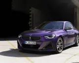 Fioletowe BMW 220i coupe z nowoczesnym designem, zaparkowane na betonowym placu przed ciemnym budynkiem.